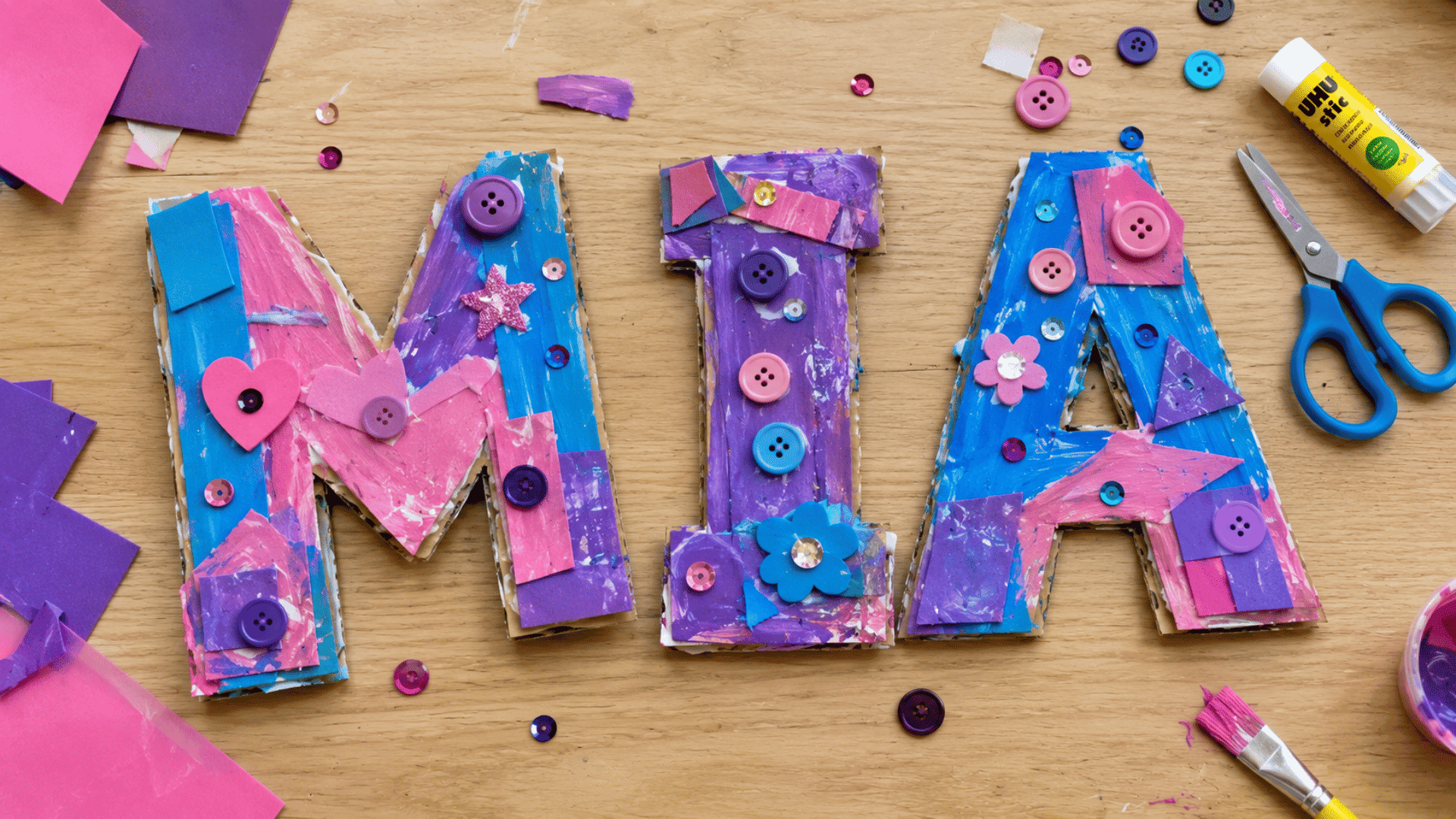 3d cardboard name art with paint buttons and sequins on light wooden table