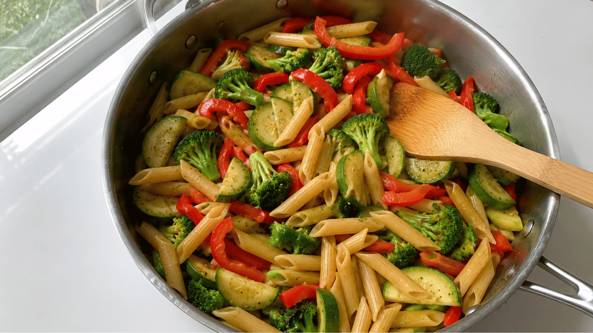 Colorful pasta with zucchini, bell pepper and broccoli in a skillet by a sunny window