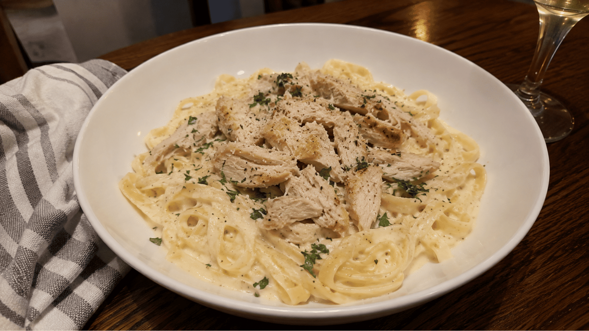 Creamy fettuccine Alfredo with pulled rotisserie chicken in a white bowl on wooden table