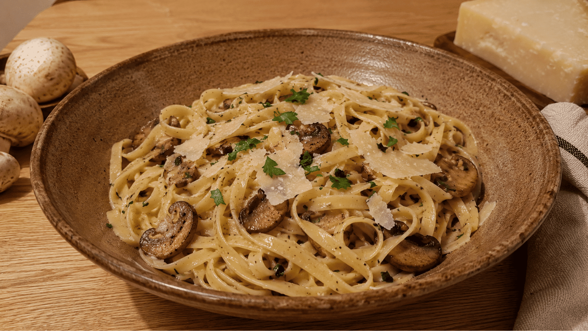 Fettuccine with browned mushrooms, shaved parmesan and parsley in a rustic ceramic bowl