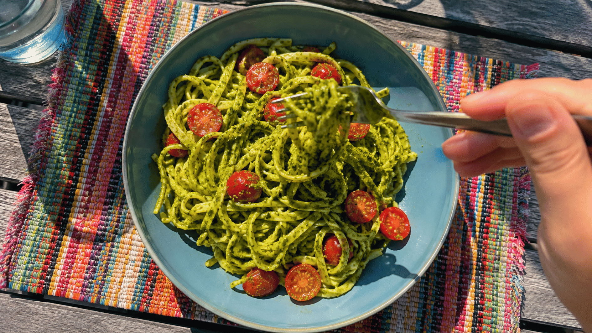 Green pesto pasta with cherry tomatoes in a blue bowl on a colorful outdoor placemat