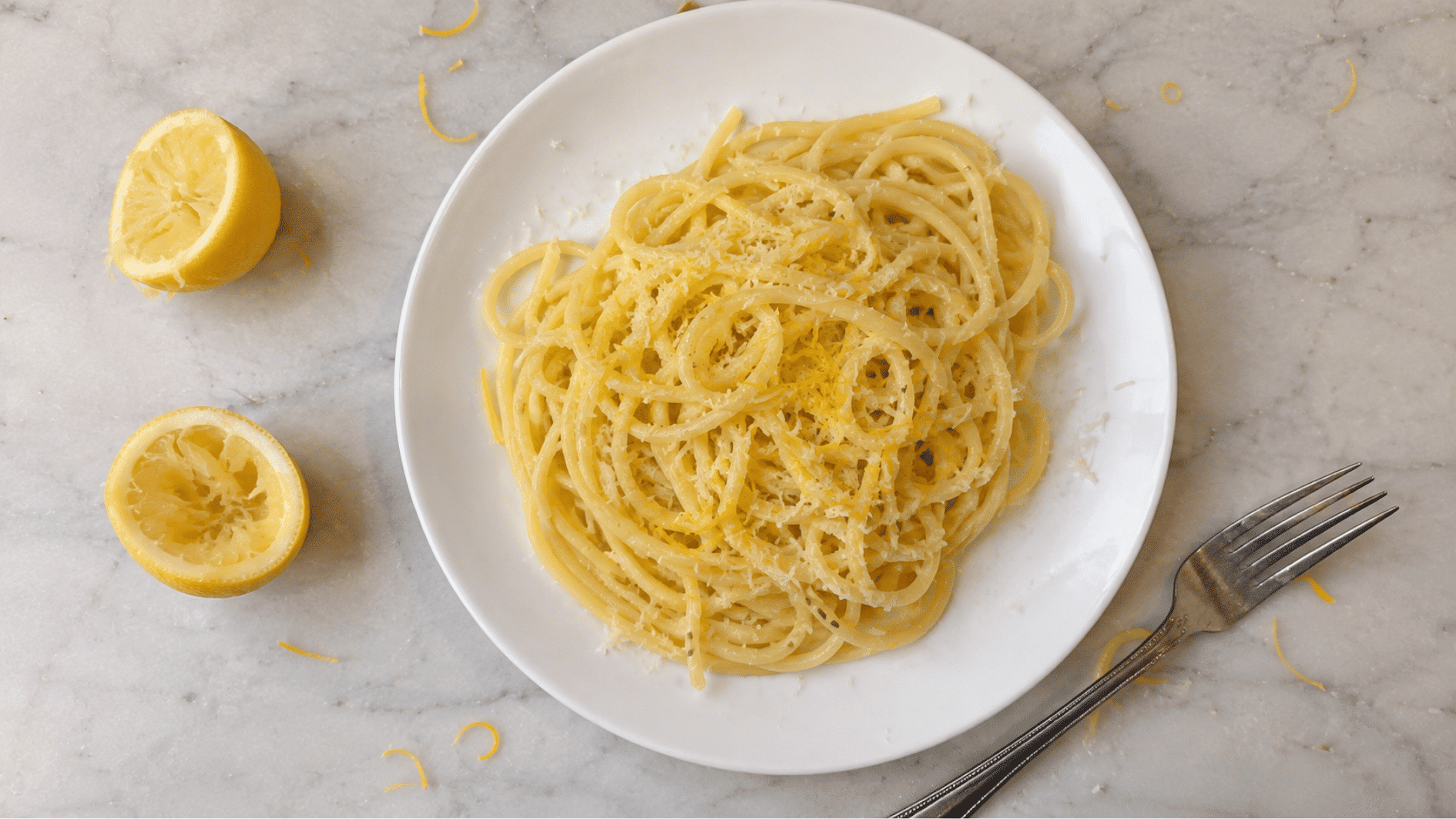 Linguine with lemon zest and grated parmesan on a white plate with lemon halves