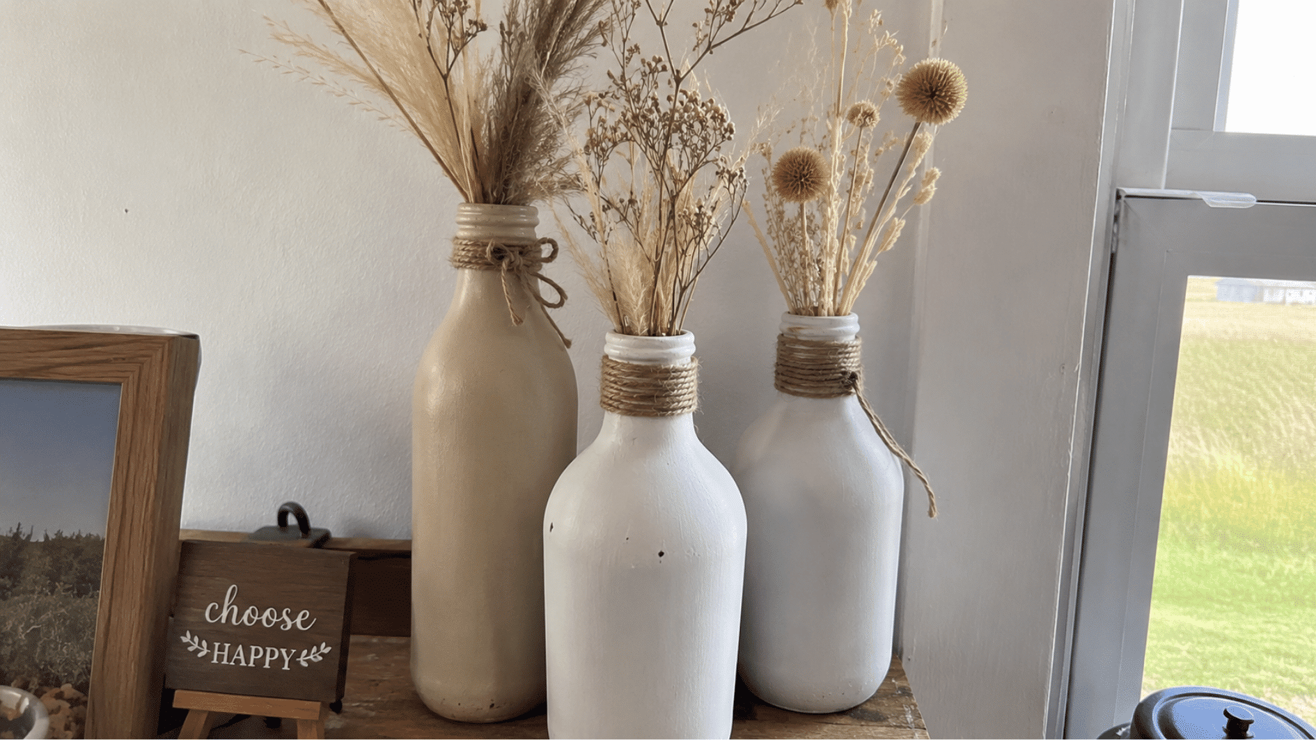 Painted glass bottle vases with dried flowers on a shelf.
