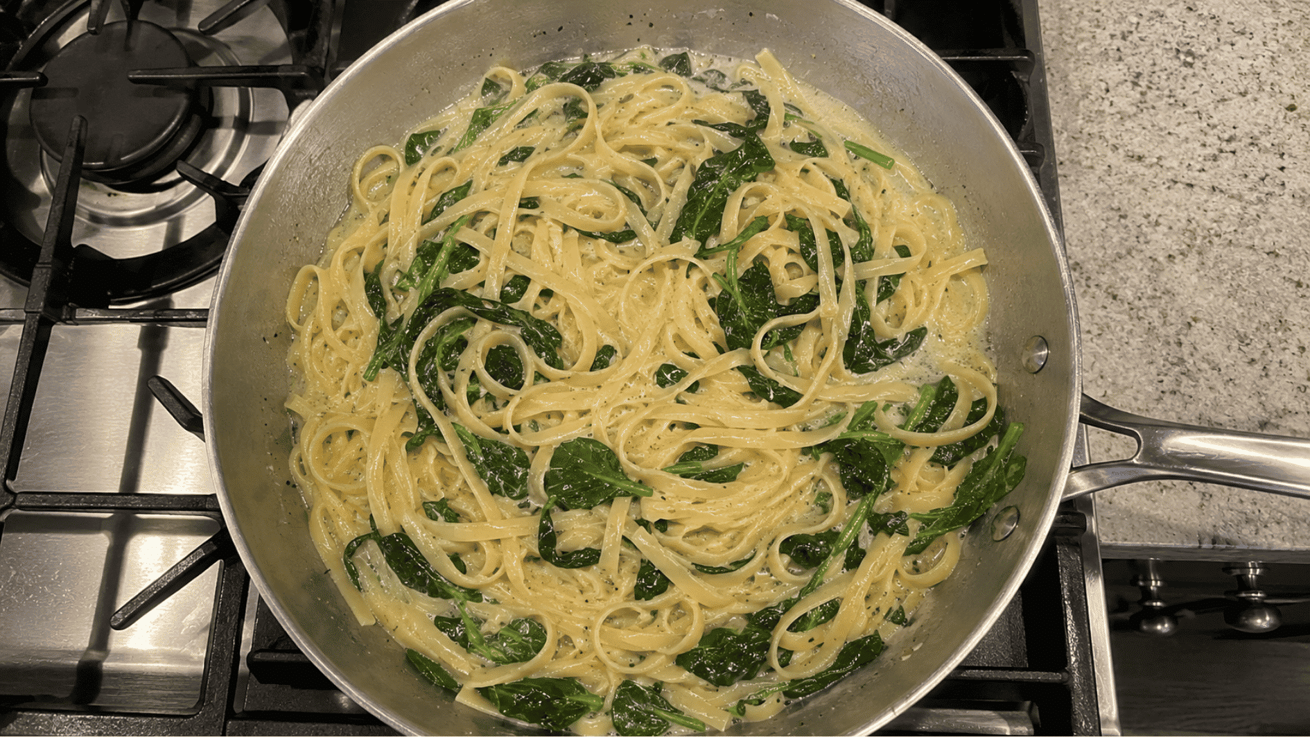 Pasta and wilted spinach in creamy sauce cooked in a stainless skillet on stovetop
