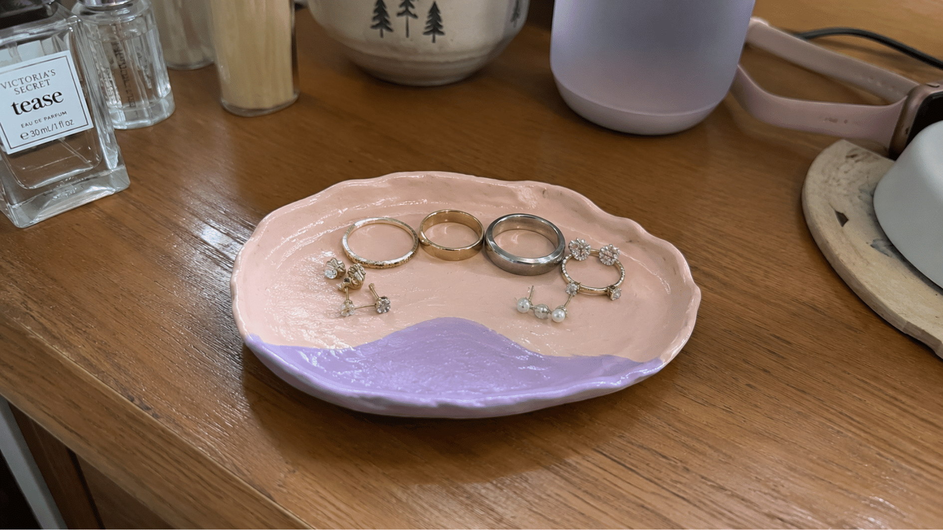 Pink clay jewelry tray holding rings and earrings on a dresser.