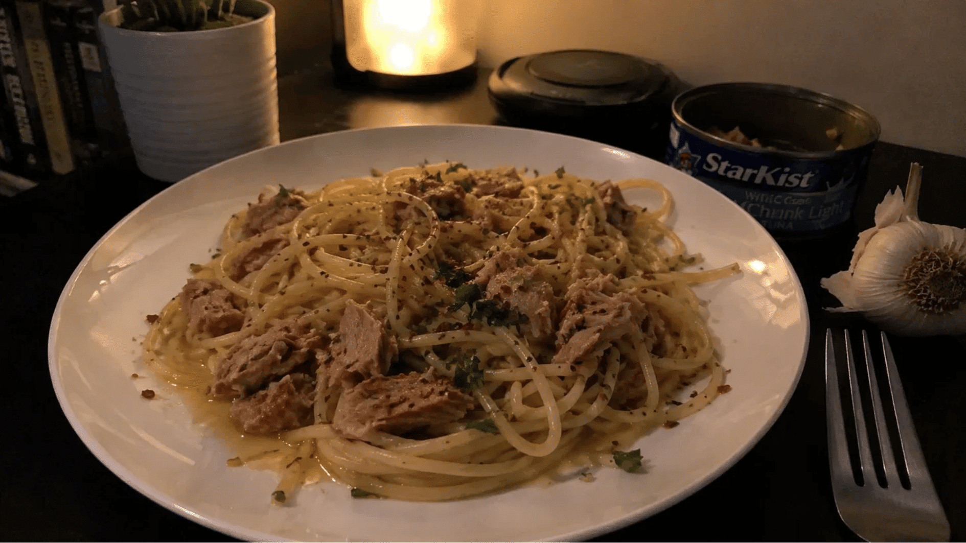 Spaghetti with chunky tuna, red pepper flakes and parsley on a plate in moody lighting
