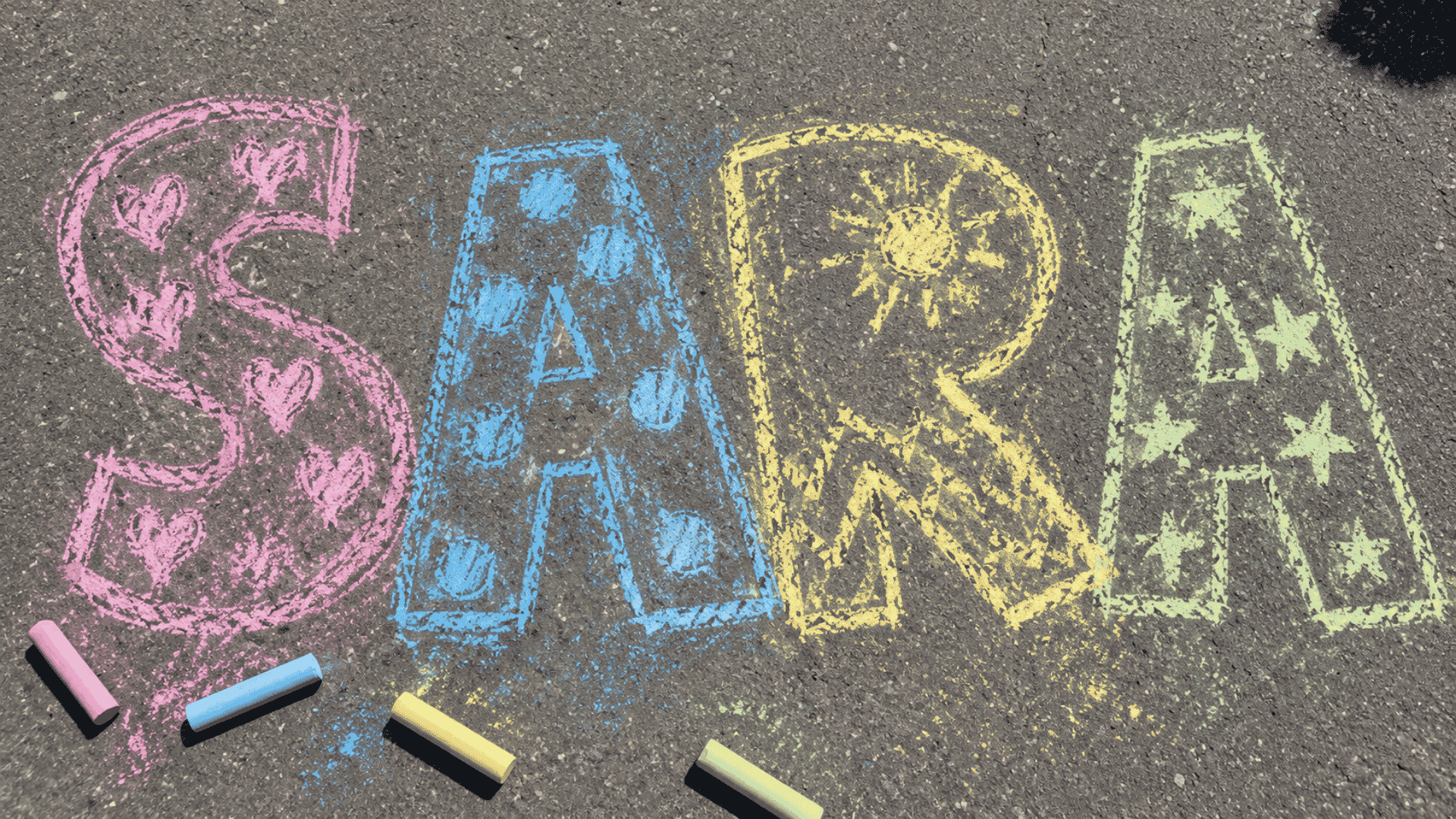 chalk name mural in pink blue yellow and green on gray asphalt driveway
