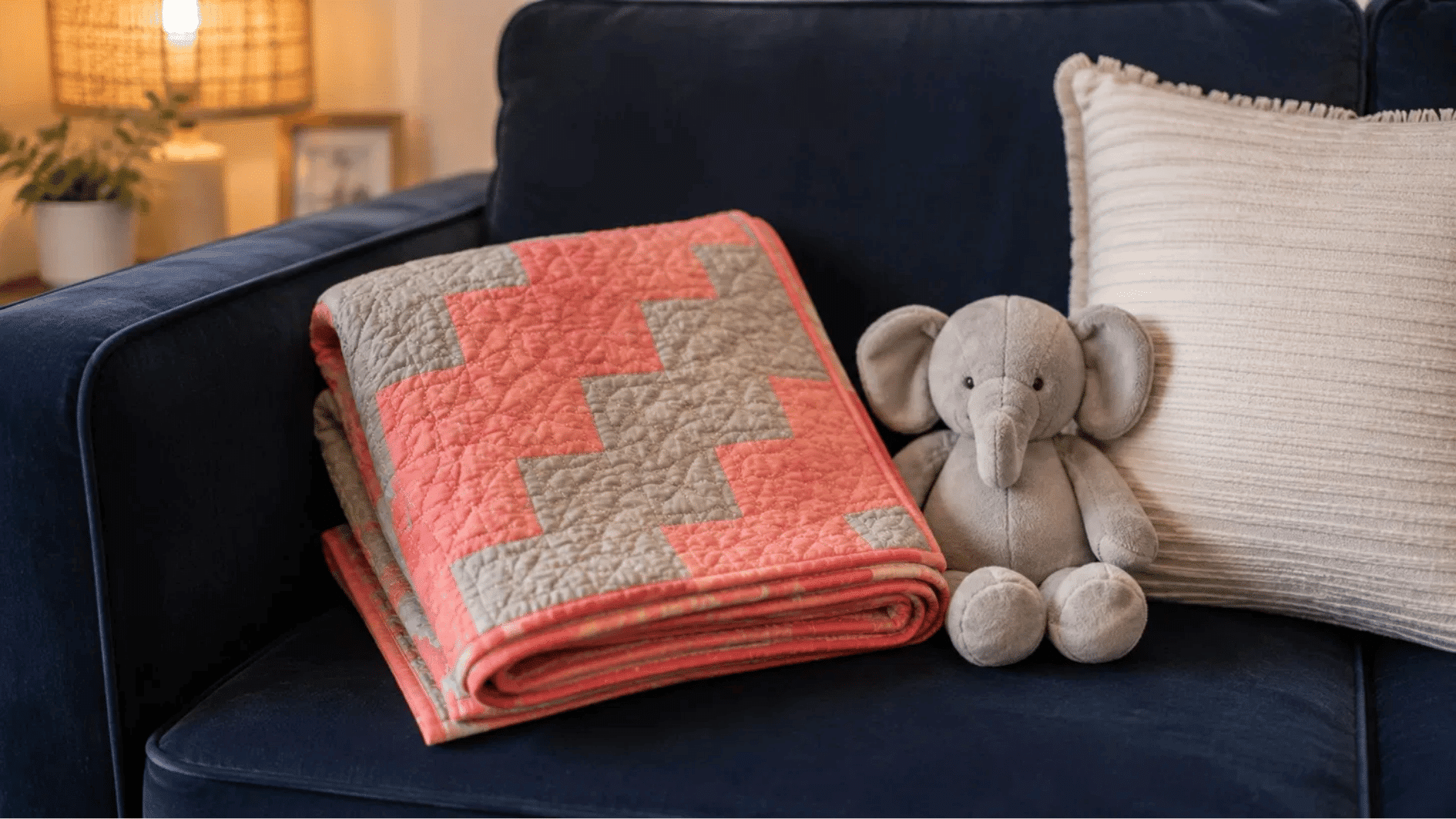 coral and grey stairway baby quilt folded on navy velvet sofa with elephant toy