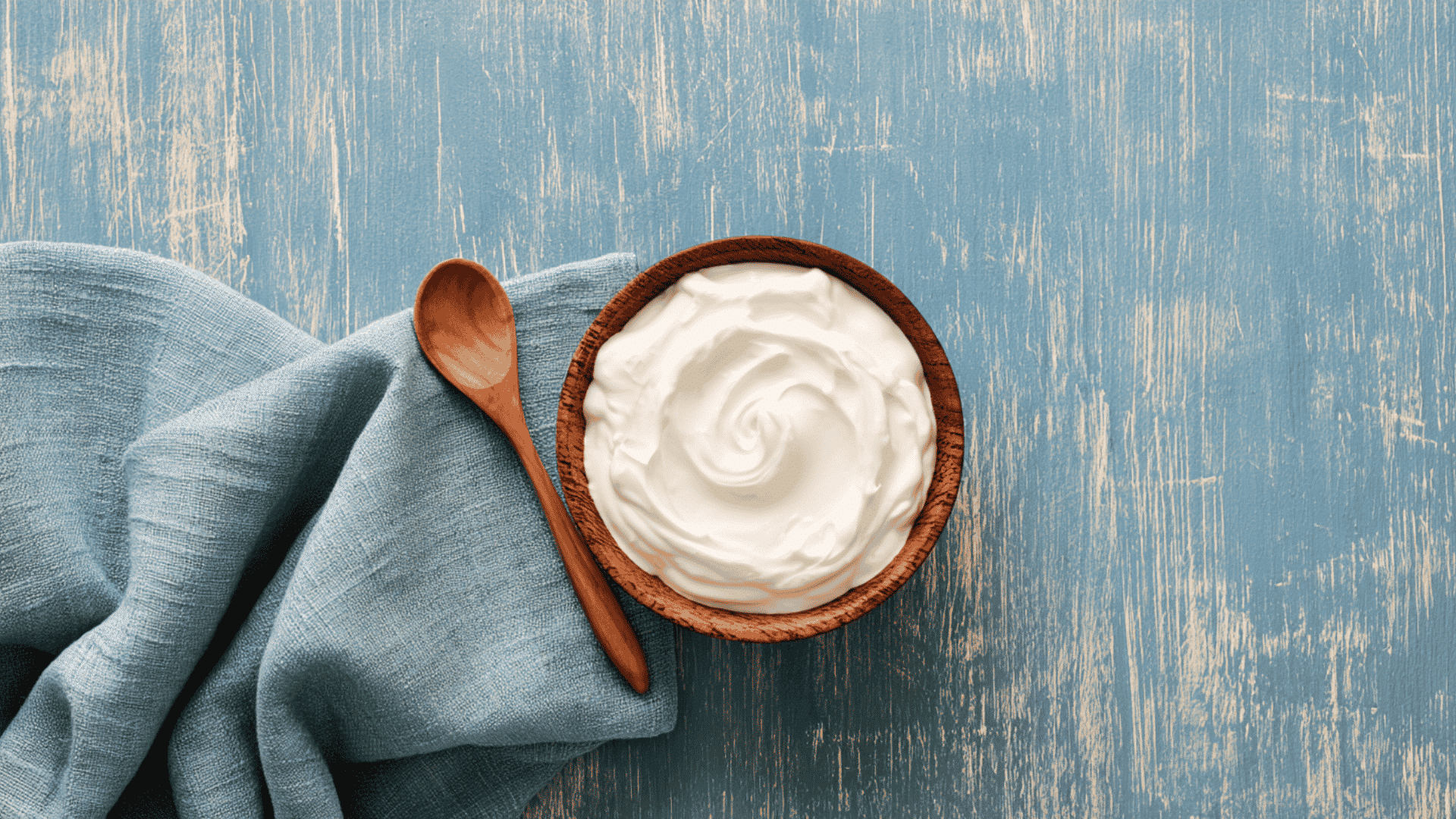 extra thick yogurt kept on a rustic blue table in wooden bowl table cloth and visible daylight