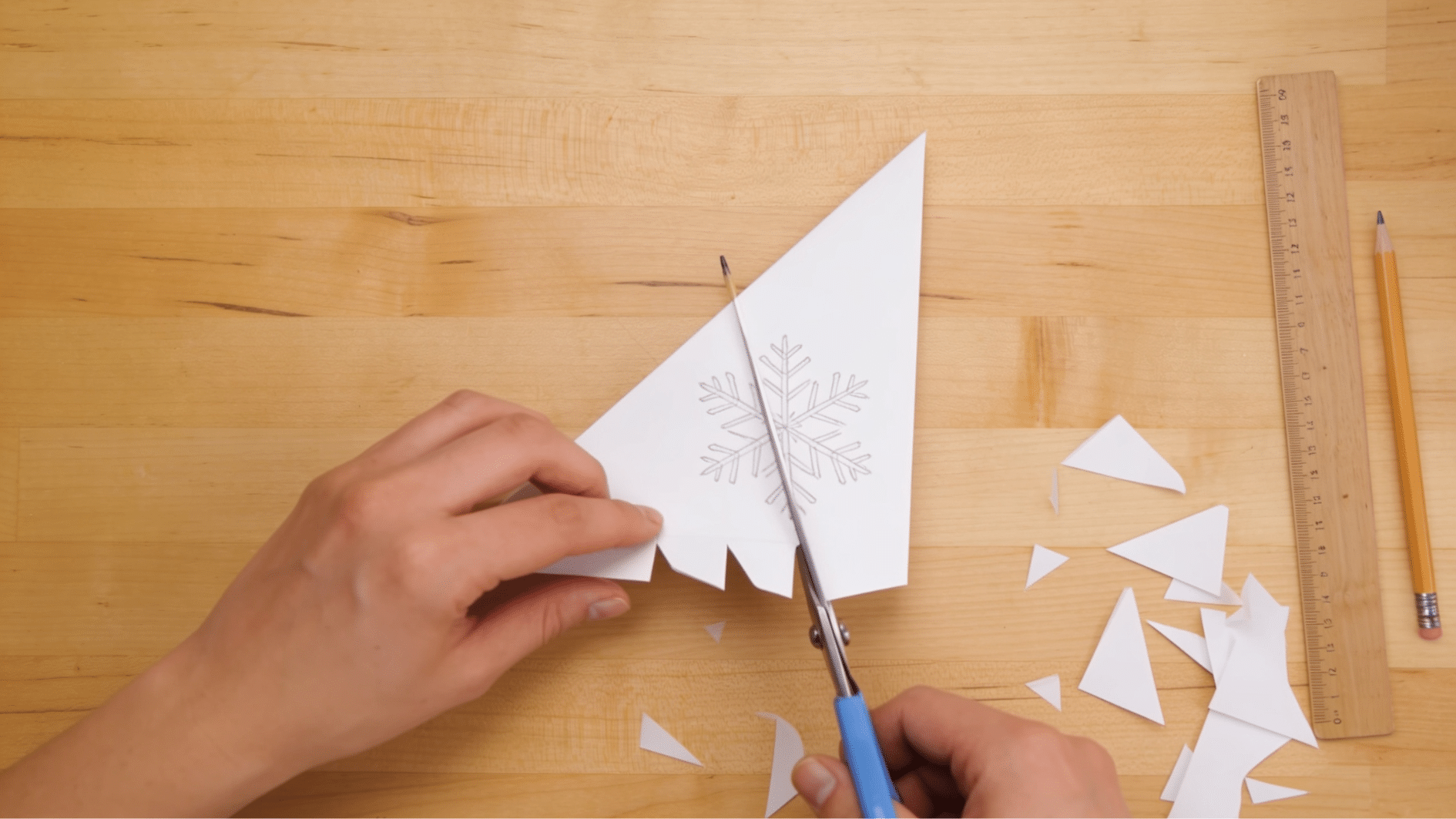 folded paper wedge with drawn pattern being cut into decorative snowflake shapes