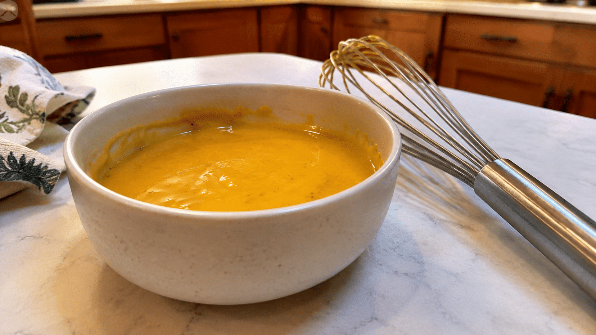 golden honey mustard sauce in a white ceramic bowl with a whisk on a marble countertop