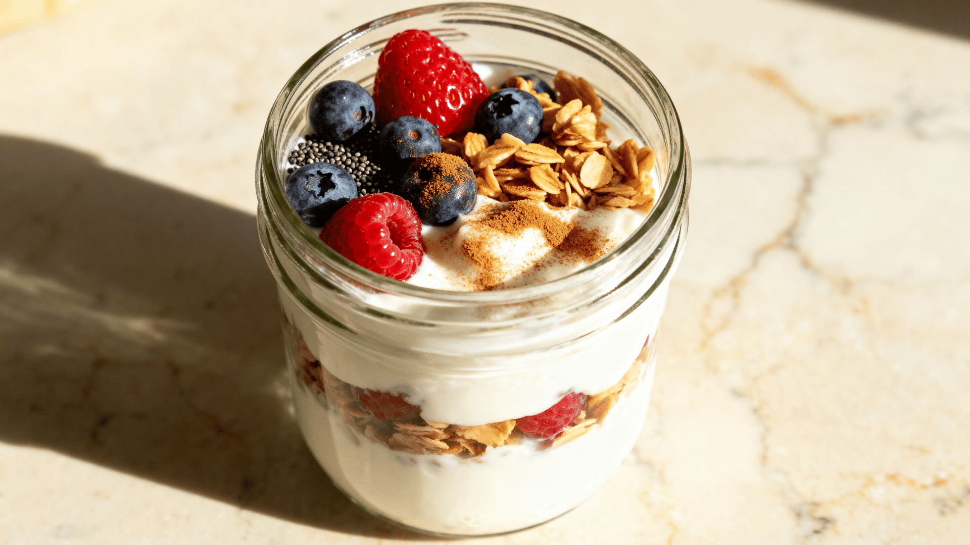 greek yogurt parfait with berries, chia seeds, granola, and cinnamon in a glass jar