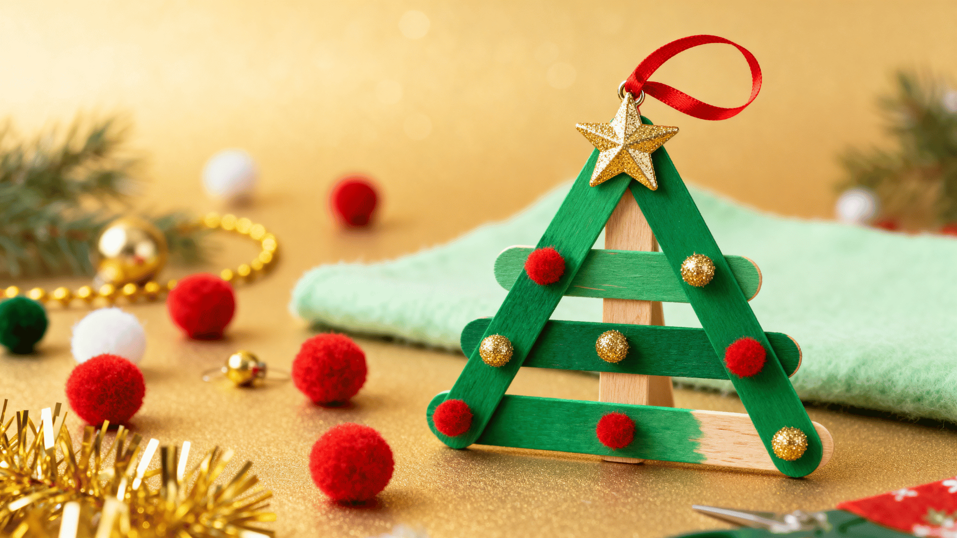 green popsicle stick christmas tree ornament with pom poms, star, and ribbon