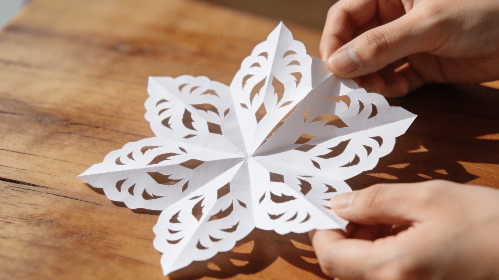 hands carefully unfolding a detailed paper snowflake revealing a six pointed design