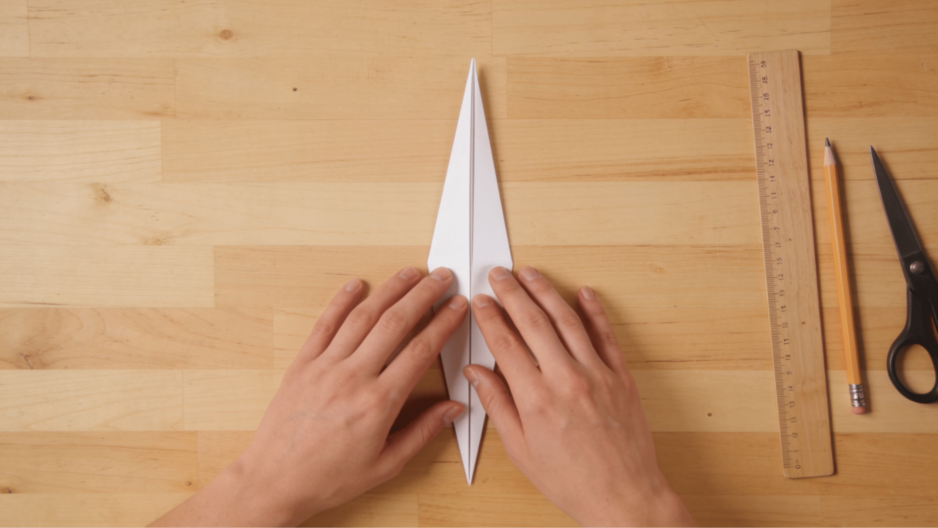 hands folding a paper triangle into thirds creating a narrow wedge shape for snowflakes