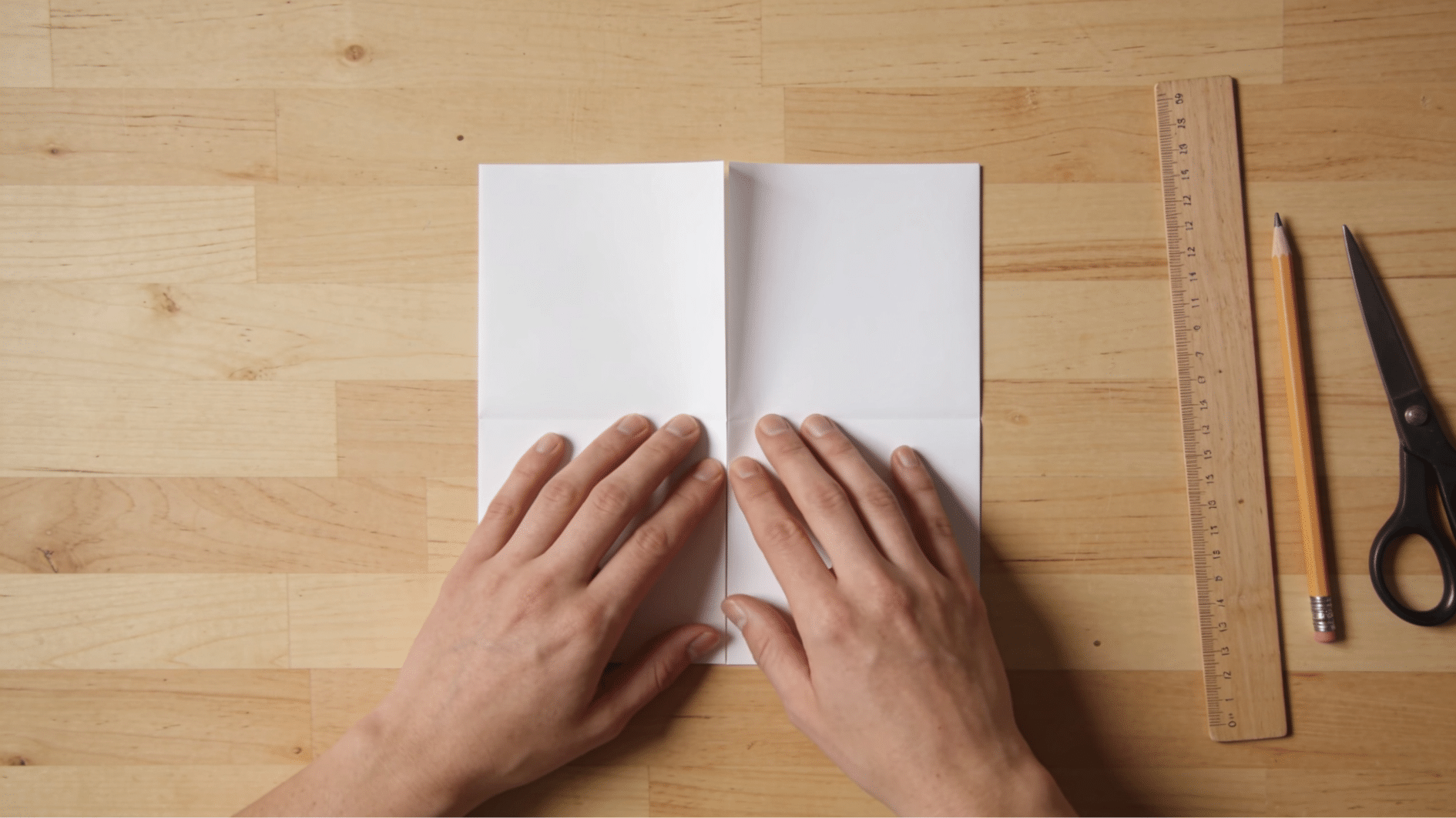 hands folding a square sheet of paper in half creating a crisp crease for snowflake craft