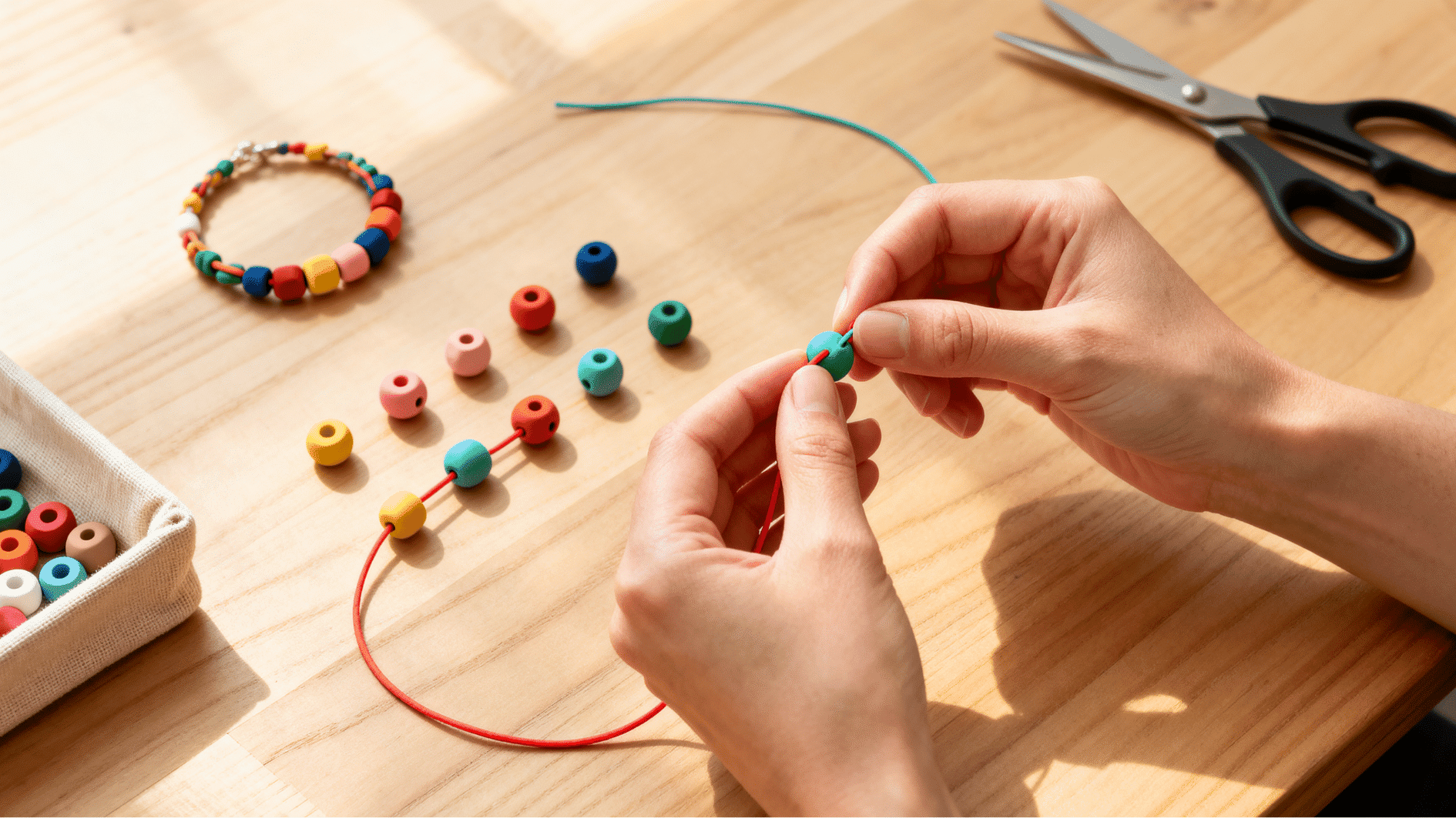 hands stringing colorful beads onto elastic cord on wooden table with scattered beads and bracelet in progress