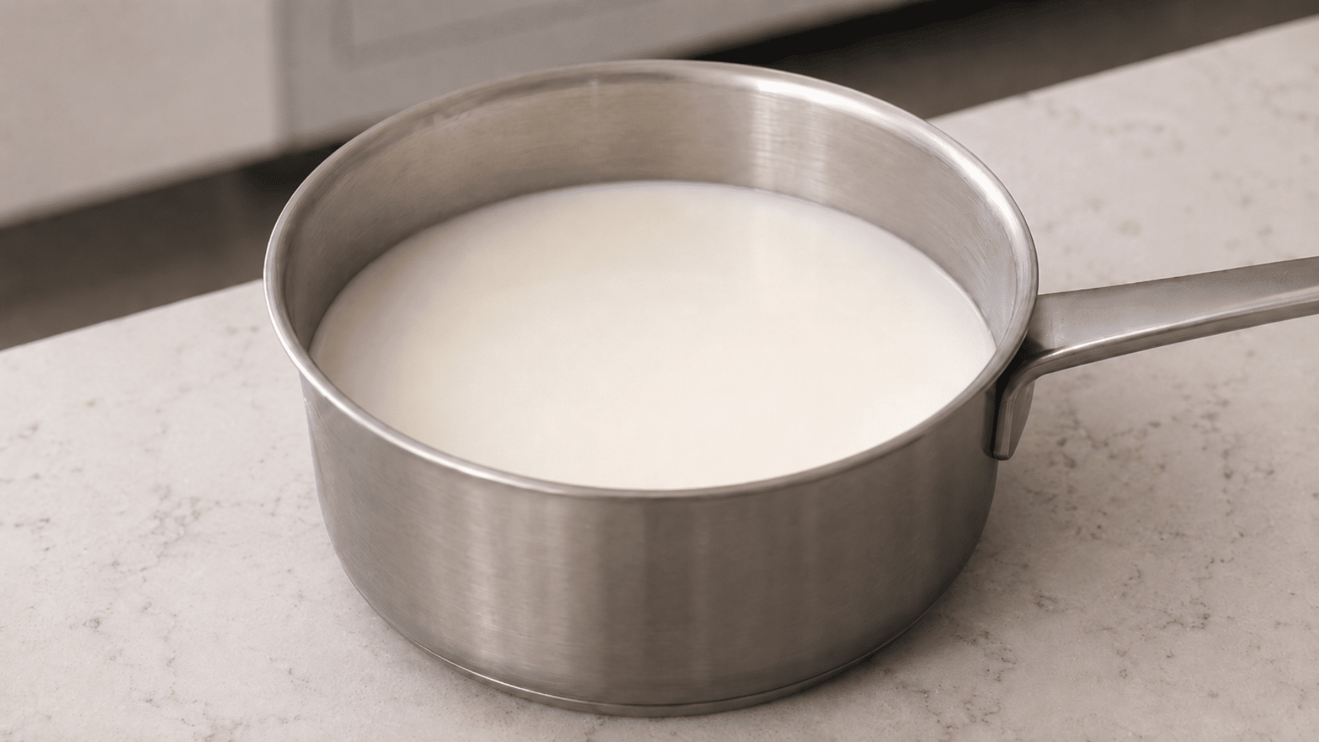 milk in a stainless steel saucepan kept on a kitchen slab for cooling after being boiled in a simple household setting with white background and blurred floor