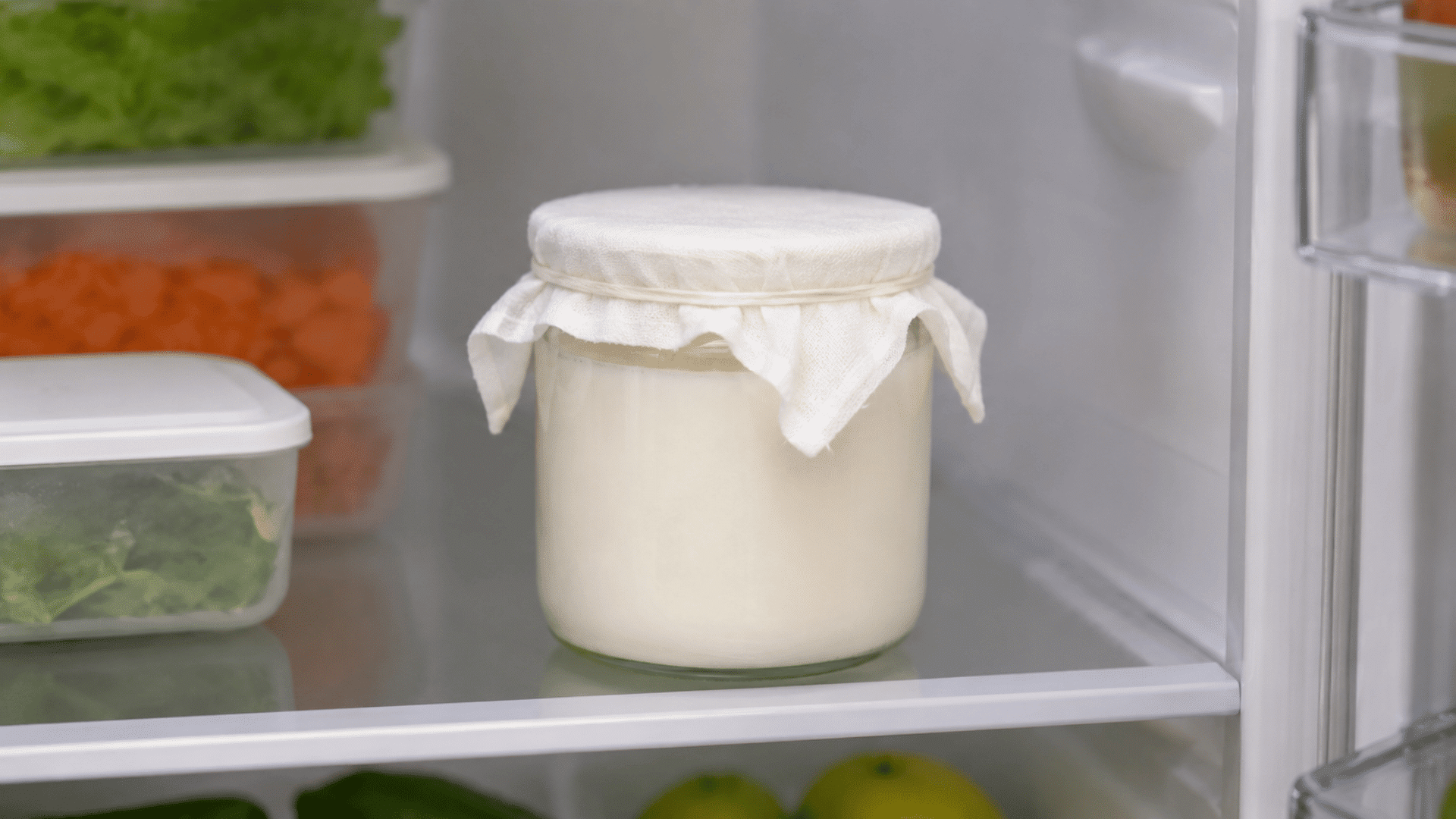milk jar in a minimal fridge interior along with vegetables visible refridgerator and jar with yogurt kept in fridge covered with white cotton cloth