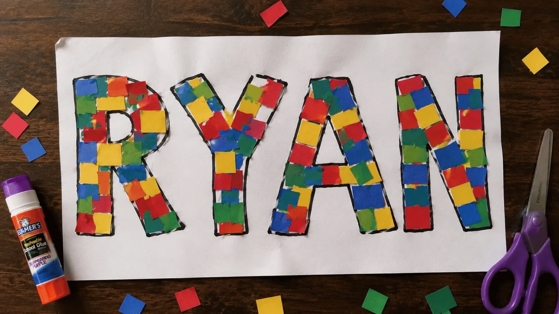 mosaic name art filled with colorful paper squares on dark wooden table