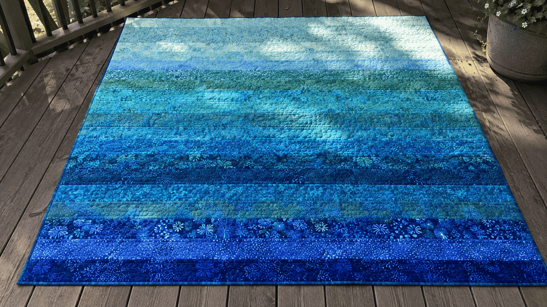 ocean-inspired batik jelly roll race quilt in blues and teals laid flat on a wooden deck