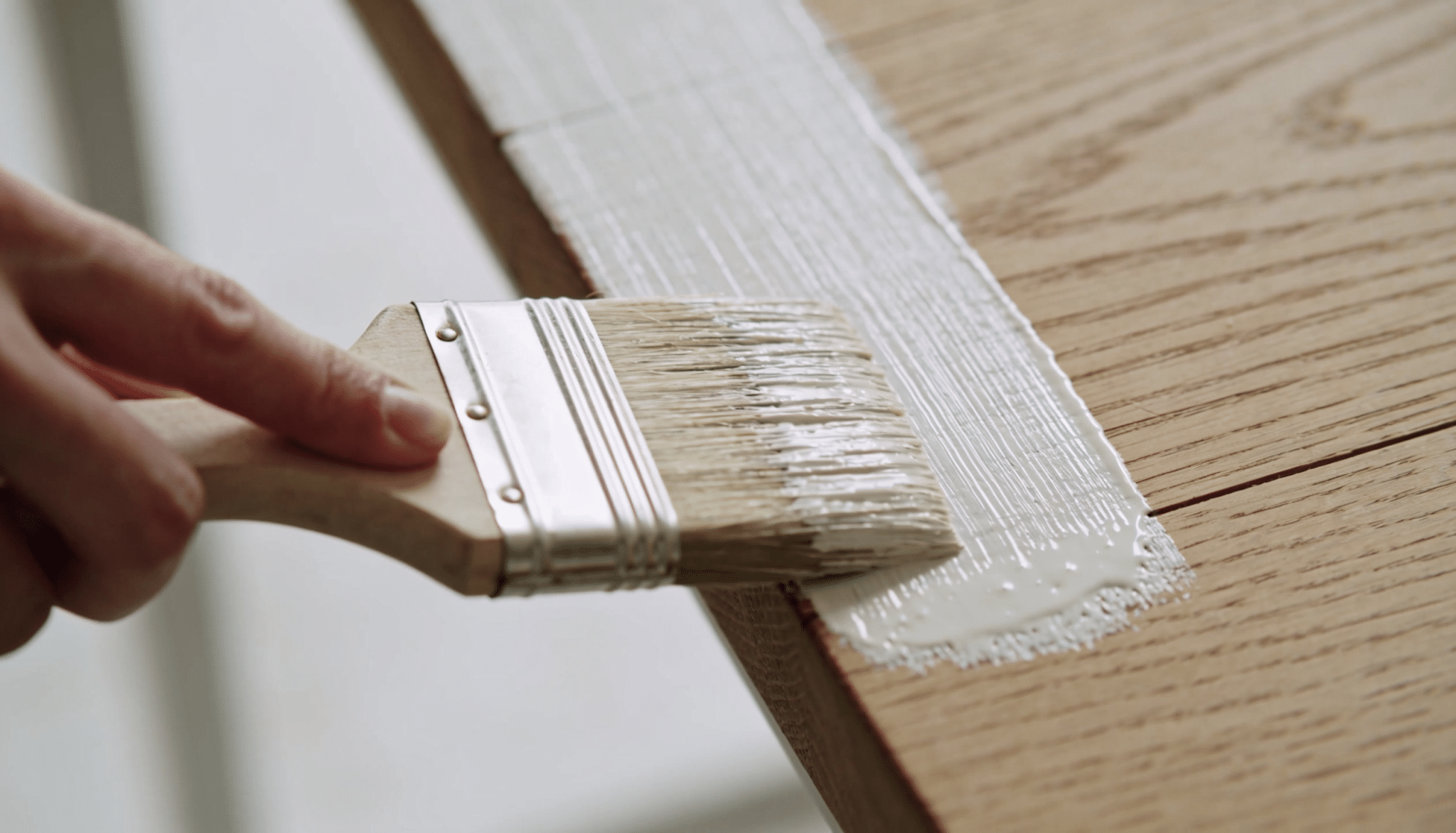 person applying a thin coat of whitewash to a wooden table with a paintbrush, following the wood grain for even coverage