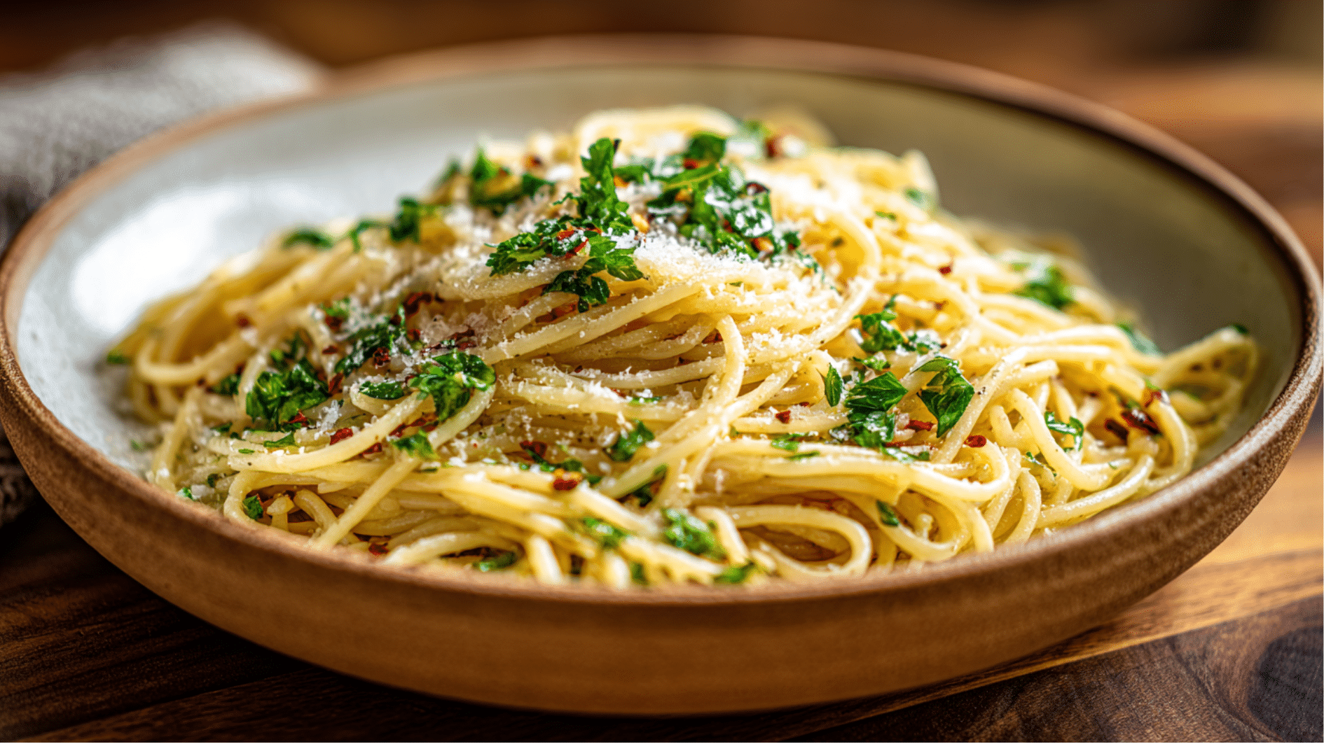 plate of spaghetti aglio e olio topped with parsley, parmesan cheese, and red pepper flakes in a rustic bowl.