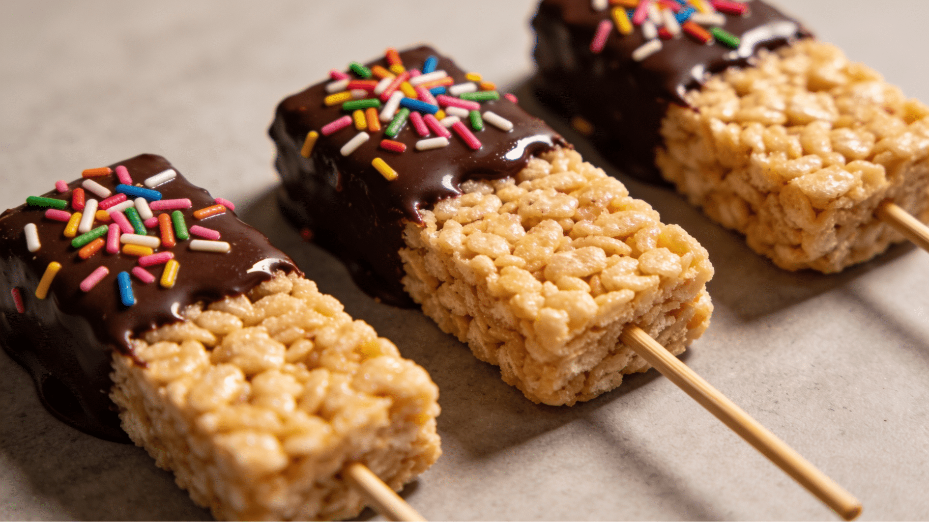 rice krispie pops dipped in white chocolate and covered with rainbow sprinkles on sticks