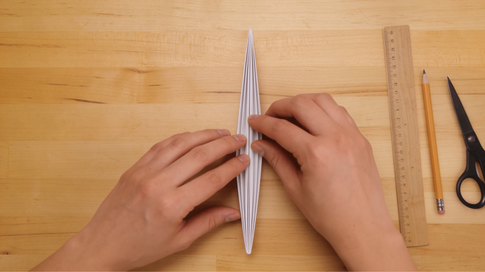 small folded paper wedge being creased in half before cutting snowflake patterns