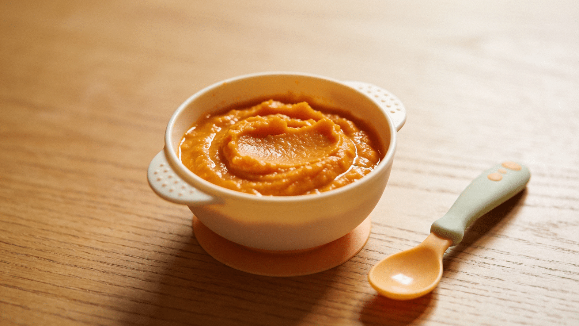 smooth sweet potato puree in a baby bowl with spoon on a wooden table in natural light