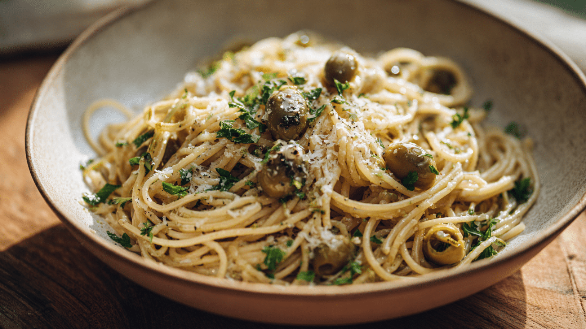 spaghetti pasta with olives, parmesan cheese, herbs, and black pepper served in a bowl on a wooden table
