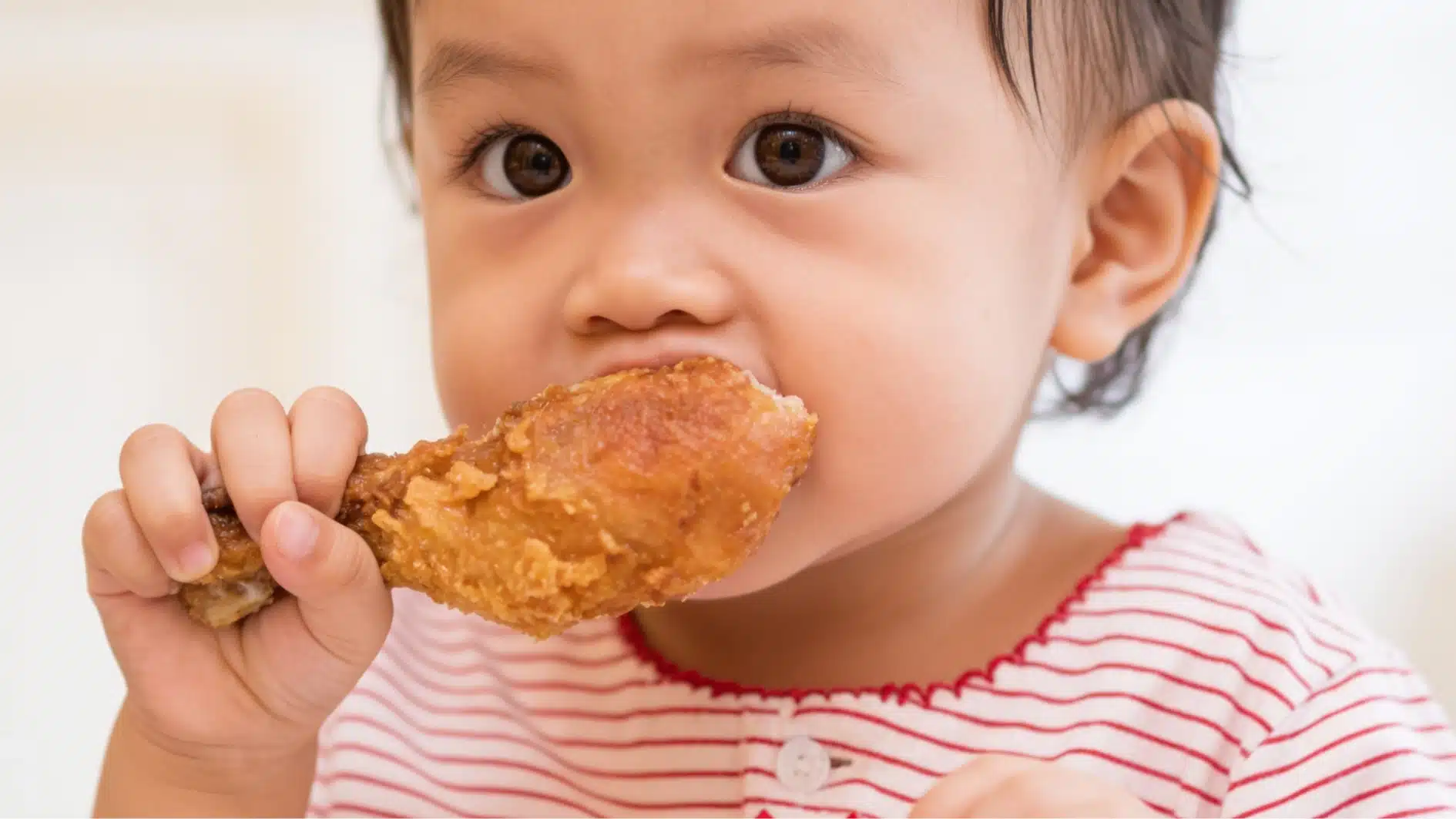 child eating fried chicken leg wearing red striped shirt