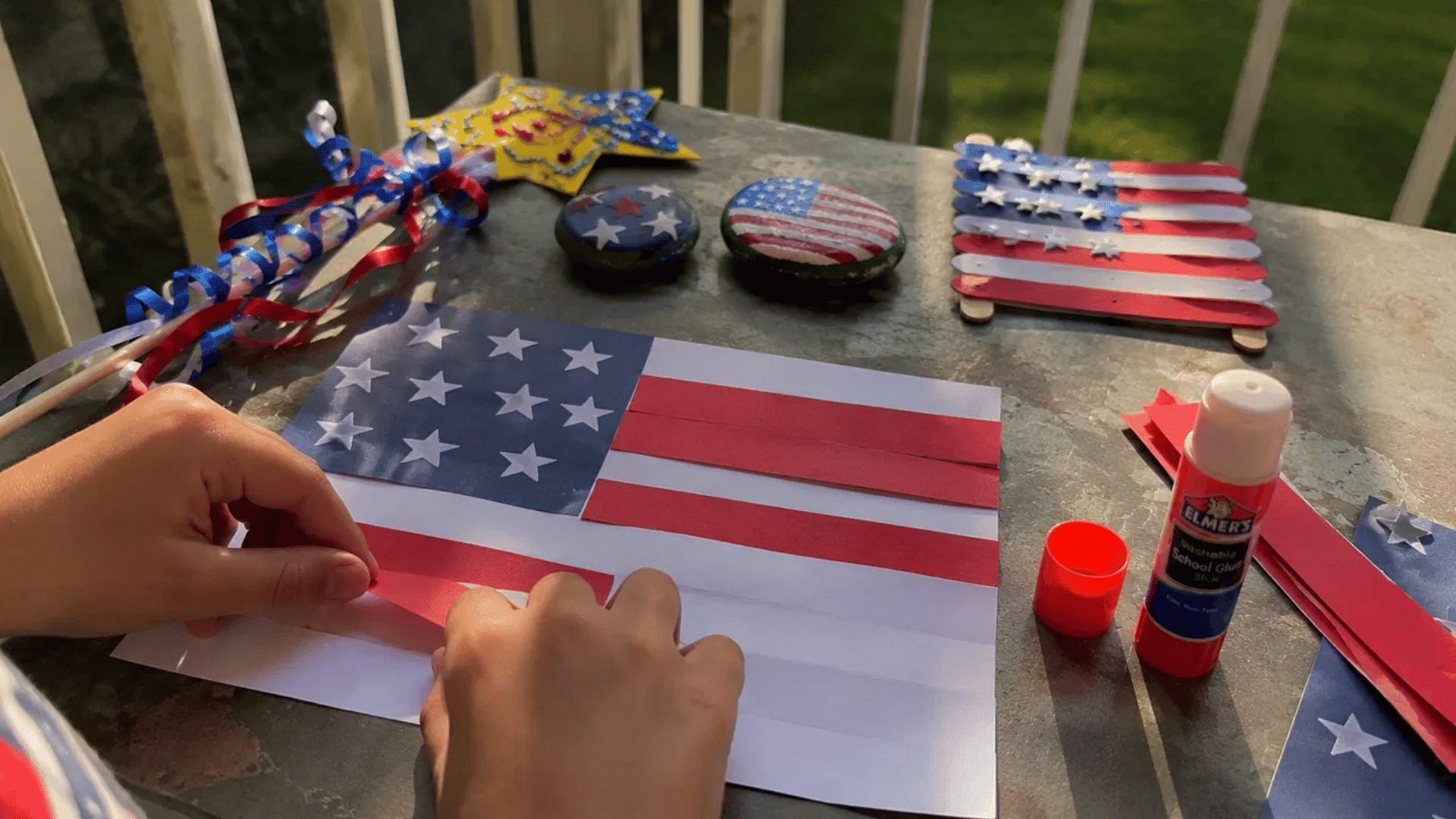 child's hands gluing a paper american flag craft with other patriotic crafts nearby