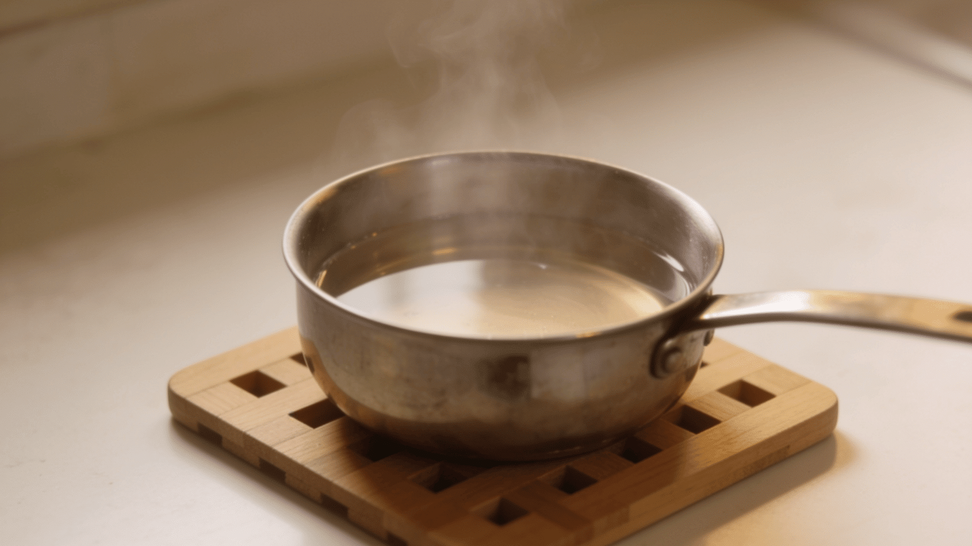 clear simple syrup cooling in a stainless steel saucepan on a wooden trivet with low steam rising over the pan