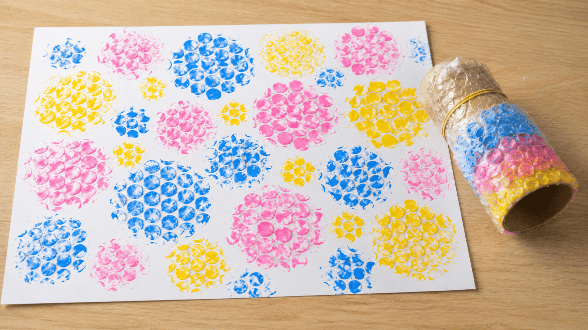 colorful bubble wrap circle prints on white paper next to a handmade stamping roll on a wooden table