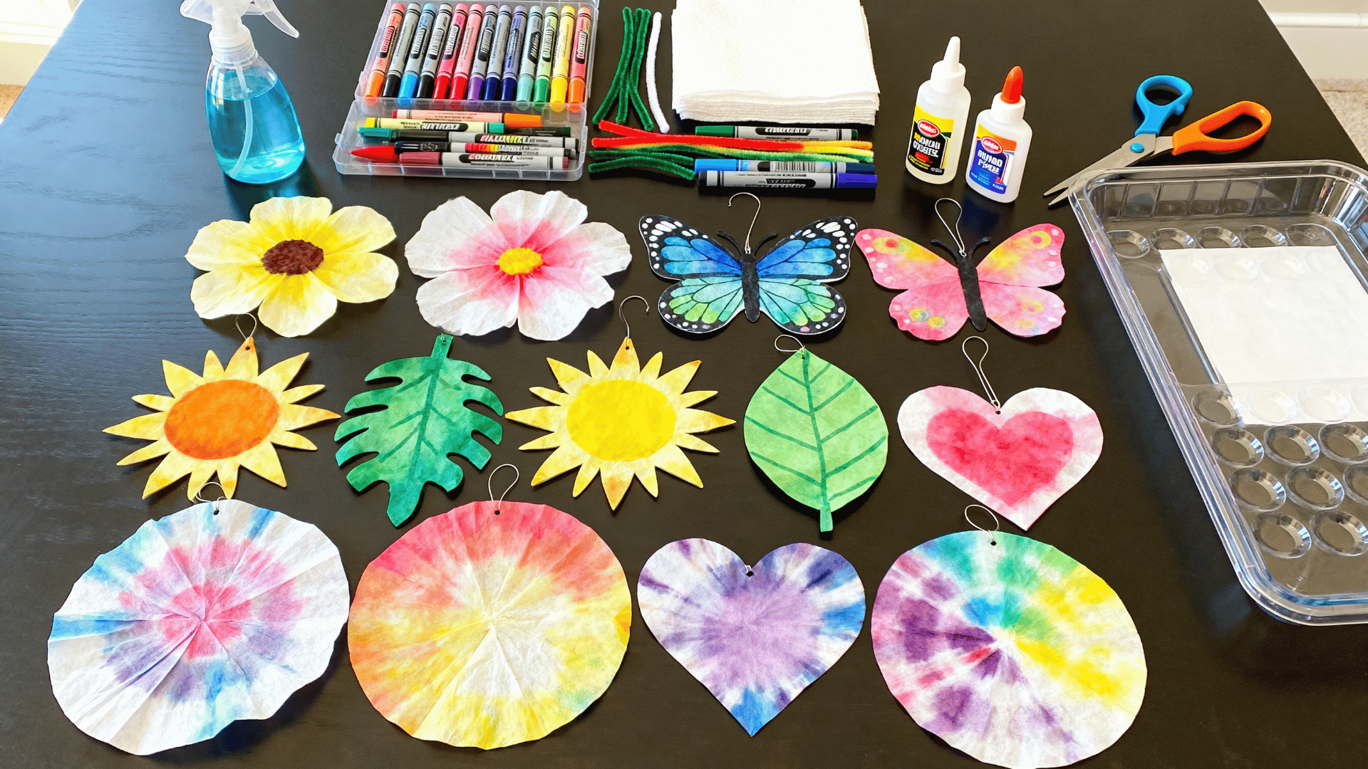 colorful coffee filter art crafts on a bright table with flowers, butterflies, hearts, markers, and craft supplies nearby