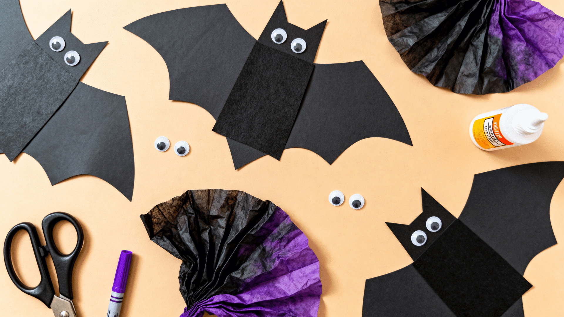 dark coffee filter bats with black paper bodies on an october craft table with scissors and purple markers nearby
