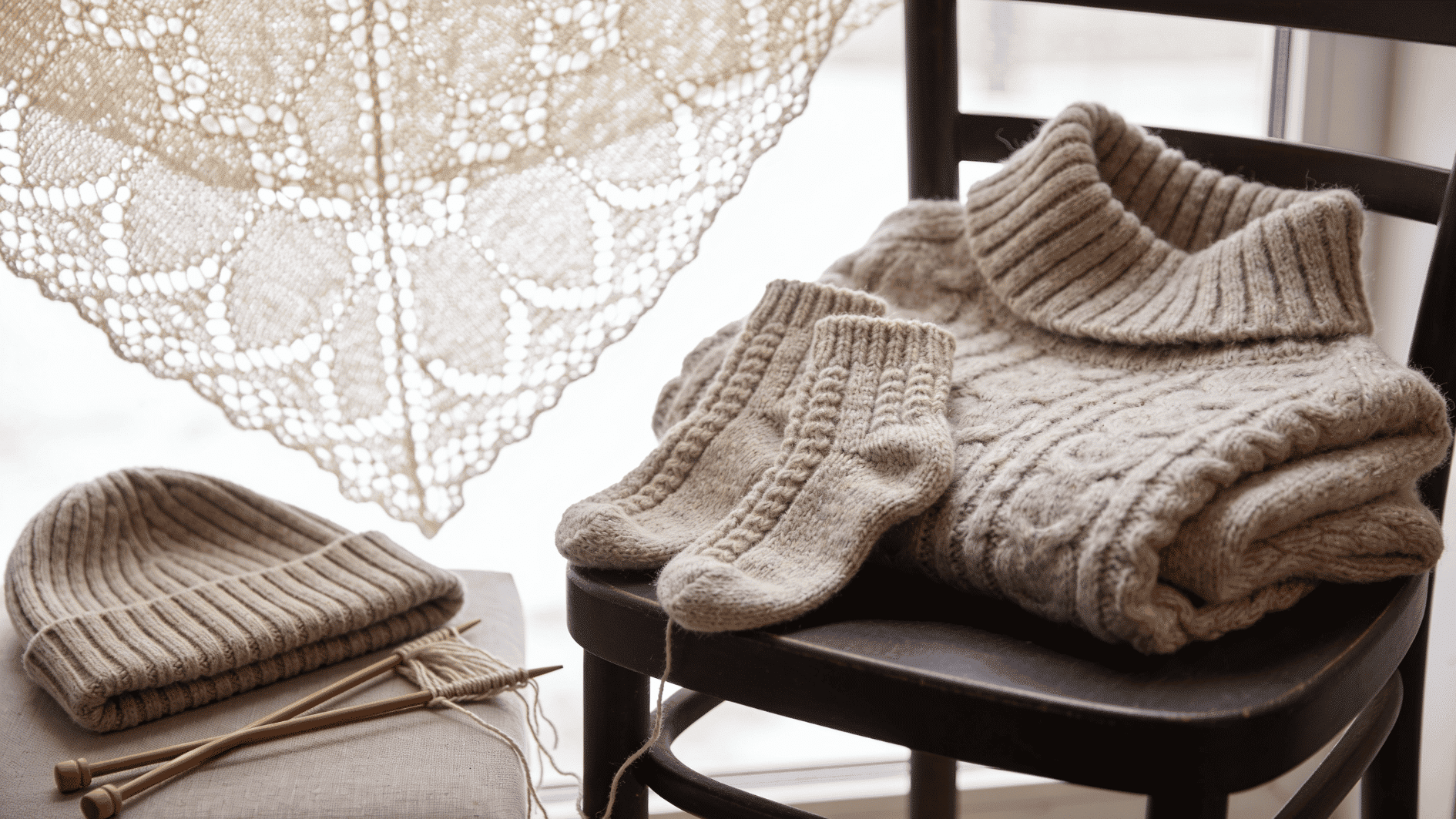 finished knitting projects draped naturally a chunky knit sweater folded over a chair, a pair of cozy knitted socks, a delicate lace shawl hanging to show its openwork pattern, and a stretchy ribb