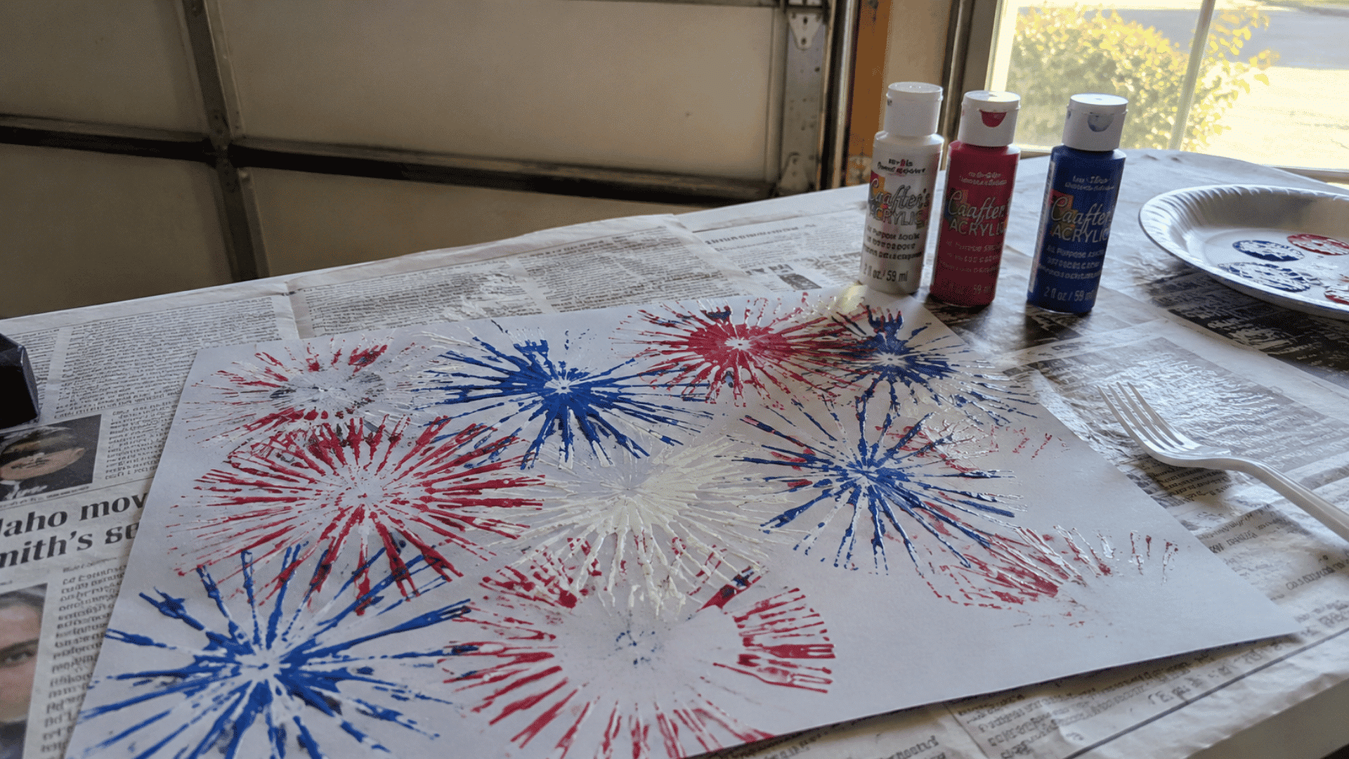 fork-stamped firework paintings in red white and blue drying on a newspaper-covered table