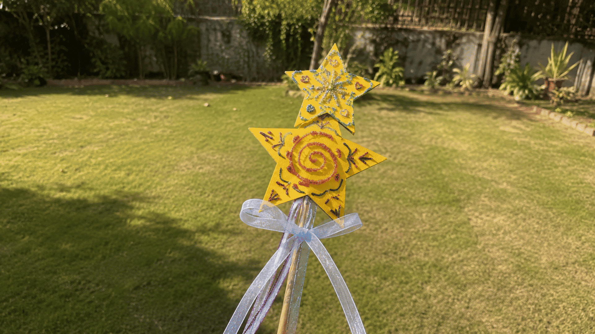 glittery yellow star wand craft with ribbon standing in a sunny backyard lawn