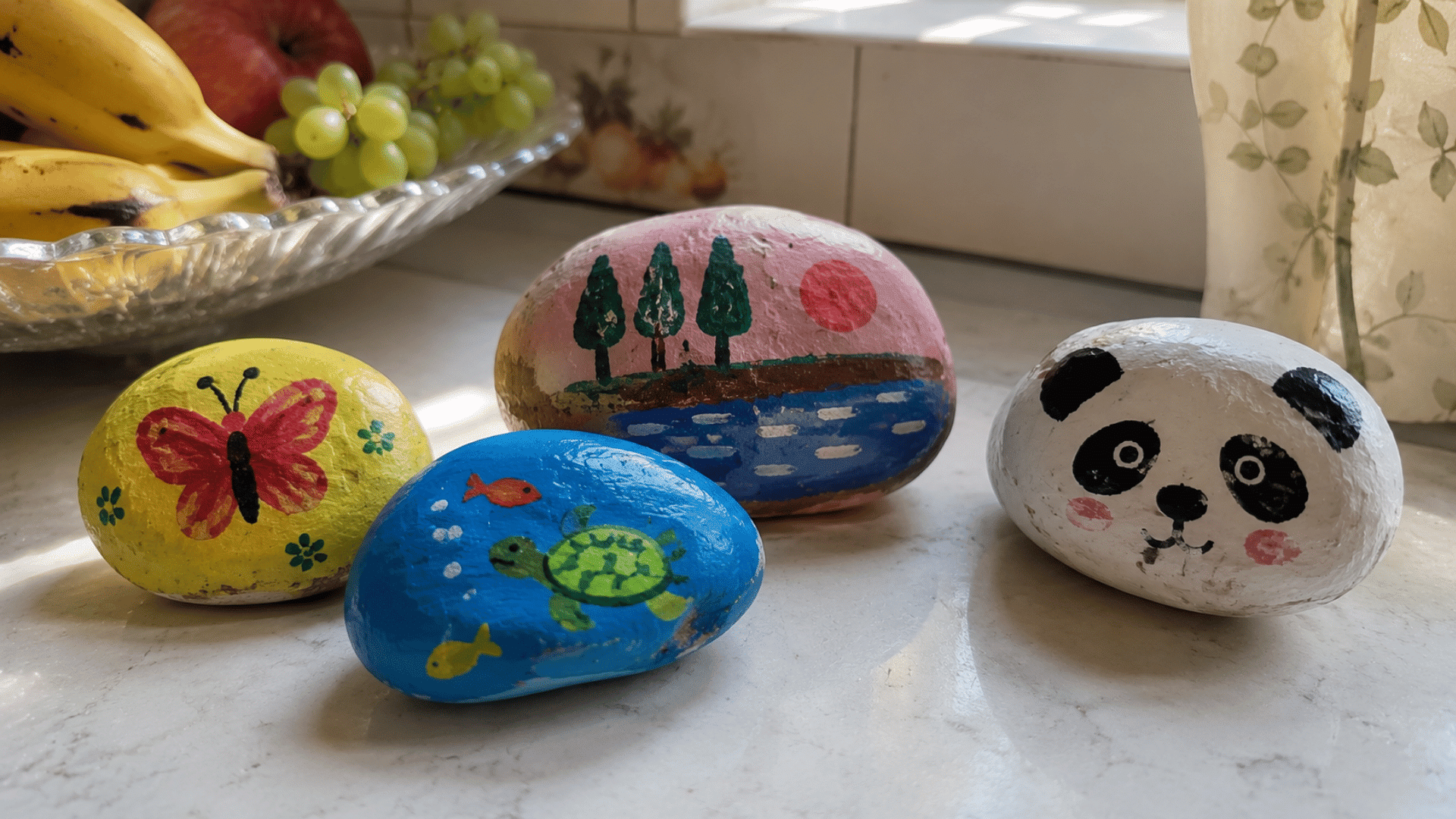 hand-painted river stones with butterfly, turtle, panda, and nature designs on kitchen counter