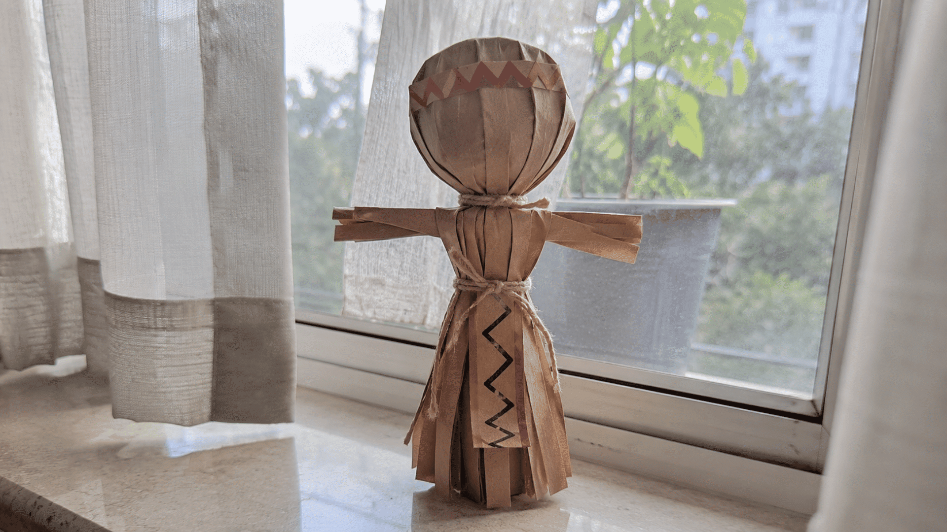 handmade brown paper corn husk doll standing on a windowsill in morning light