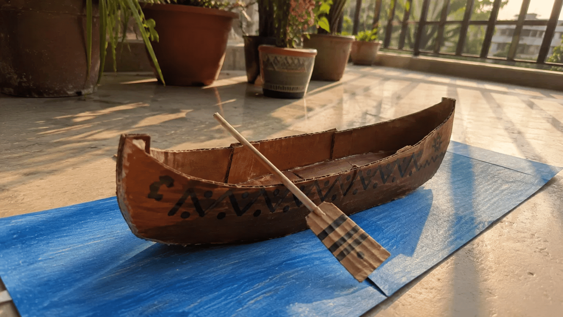 handmade cardboard canoe craft on blue paper river on a sunlit balcony
