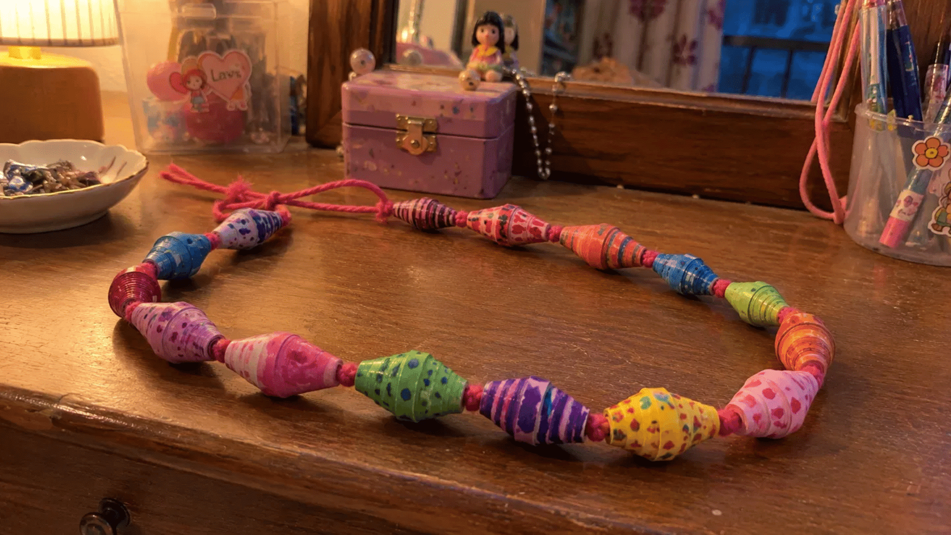 handmade colorful paper bead necklace on a wooden dresser lit by warm lamp light