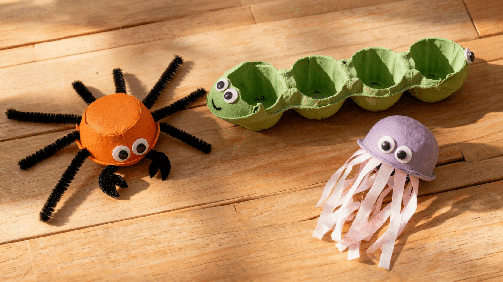 handmade craft creatures on wooden surface including orange spider, green caterpillar, and purple jellyfish (1)