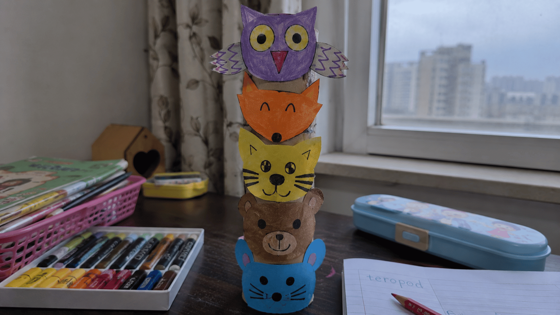 handmade paper totem pole craft with colorful animal faces on a child's study desk