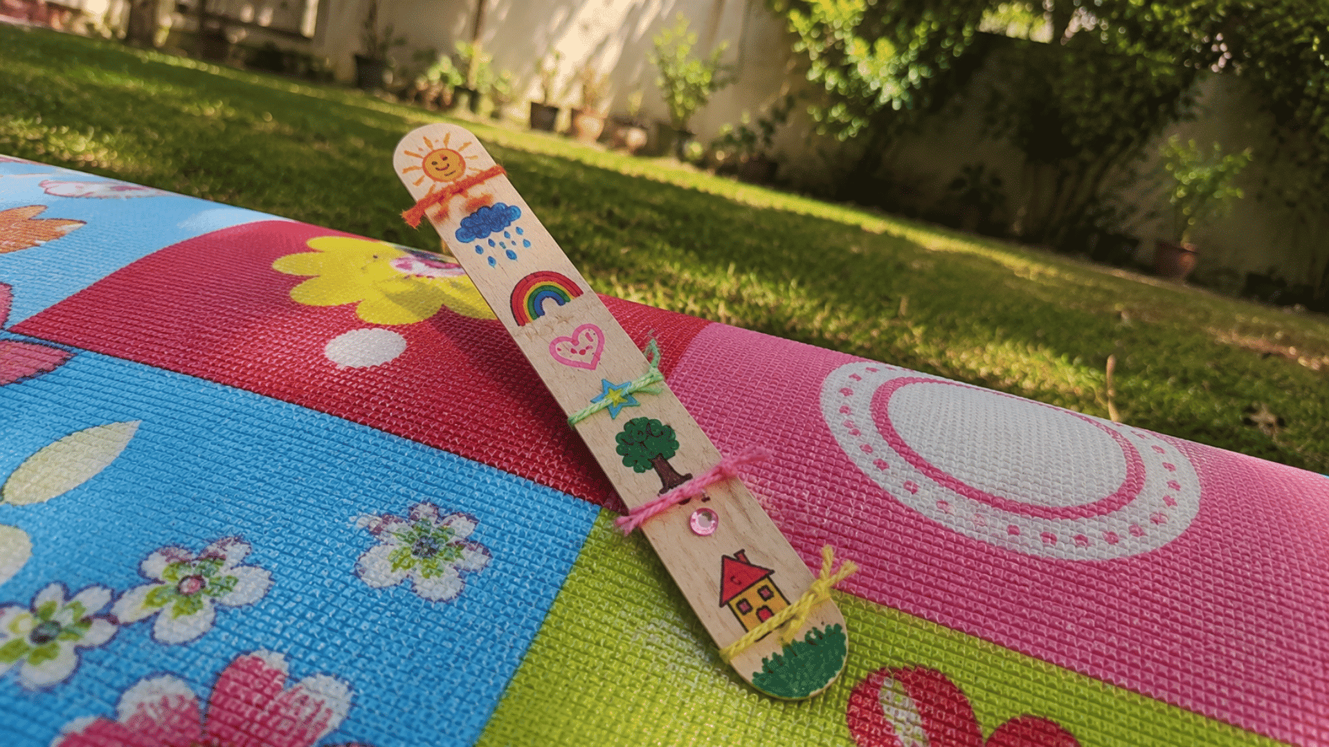 handmade wooden story stick with marker drawings standing on a colorful picnic mat outdoors