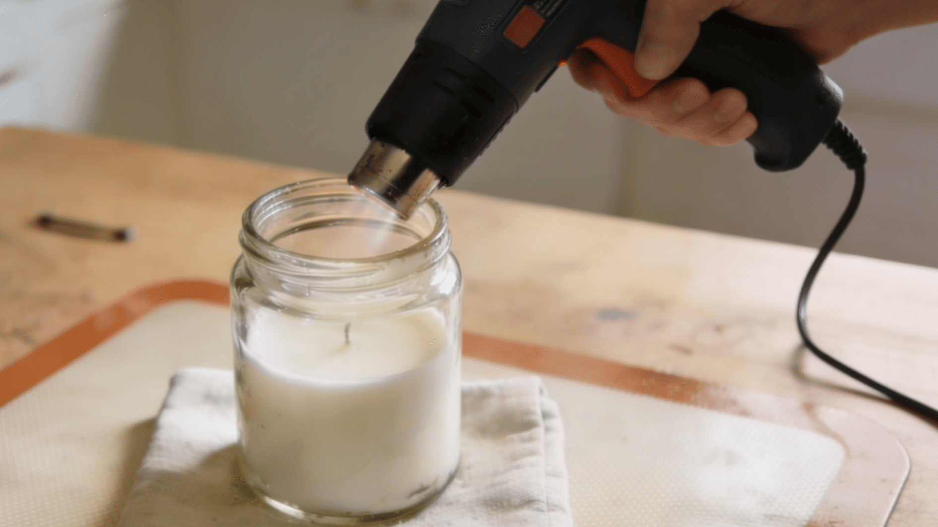heat gun warming a candle jar to soften stuck wax residue for easy removal from the surface