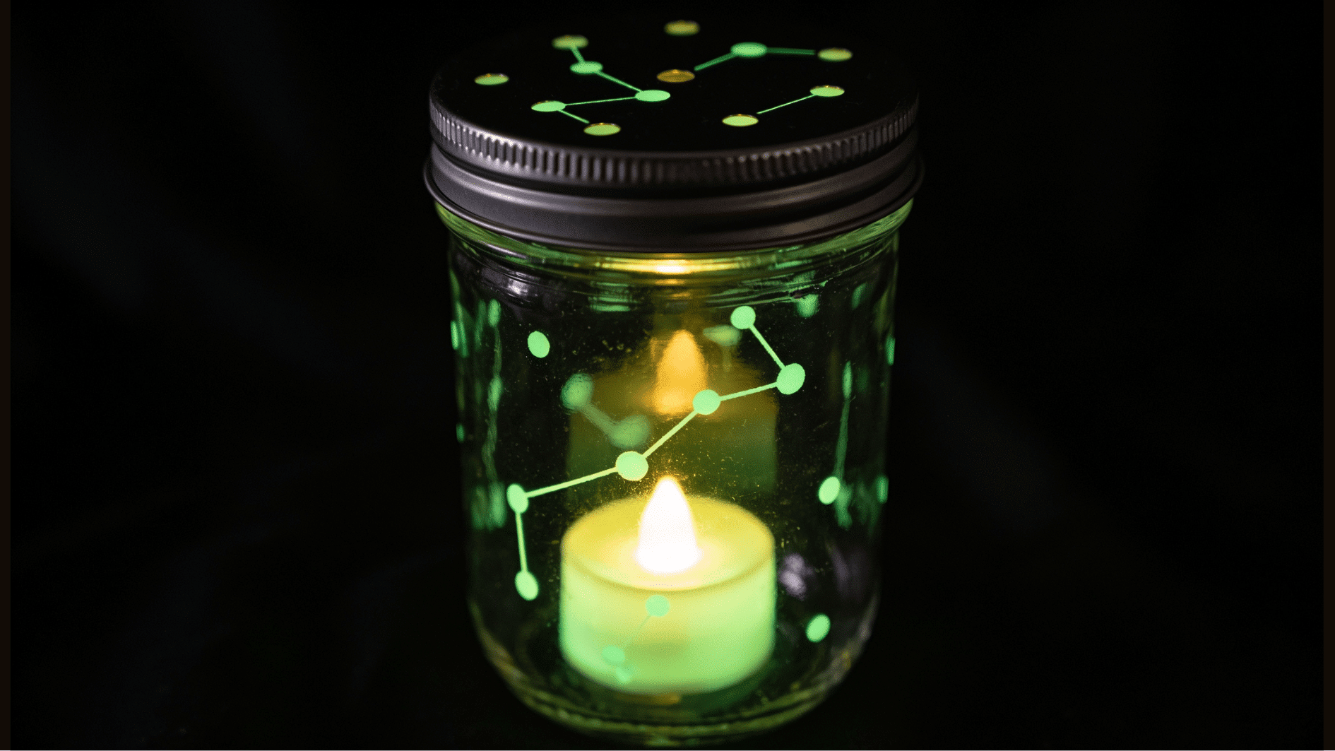 _mason jar craft with a constellation of small punched holes in the lid, glowing softly from green glow-in-the-dark paint inside, lit by a tiny tea light, photographed in a dark room.