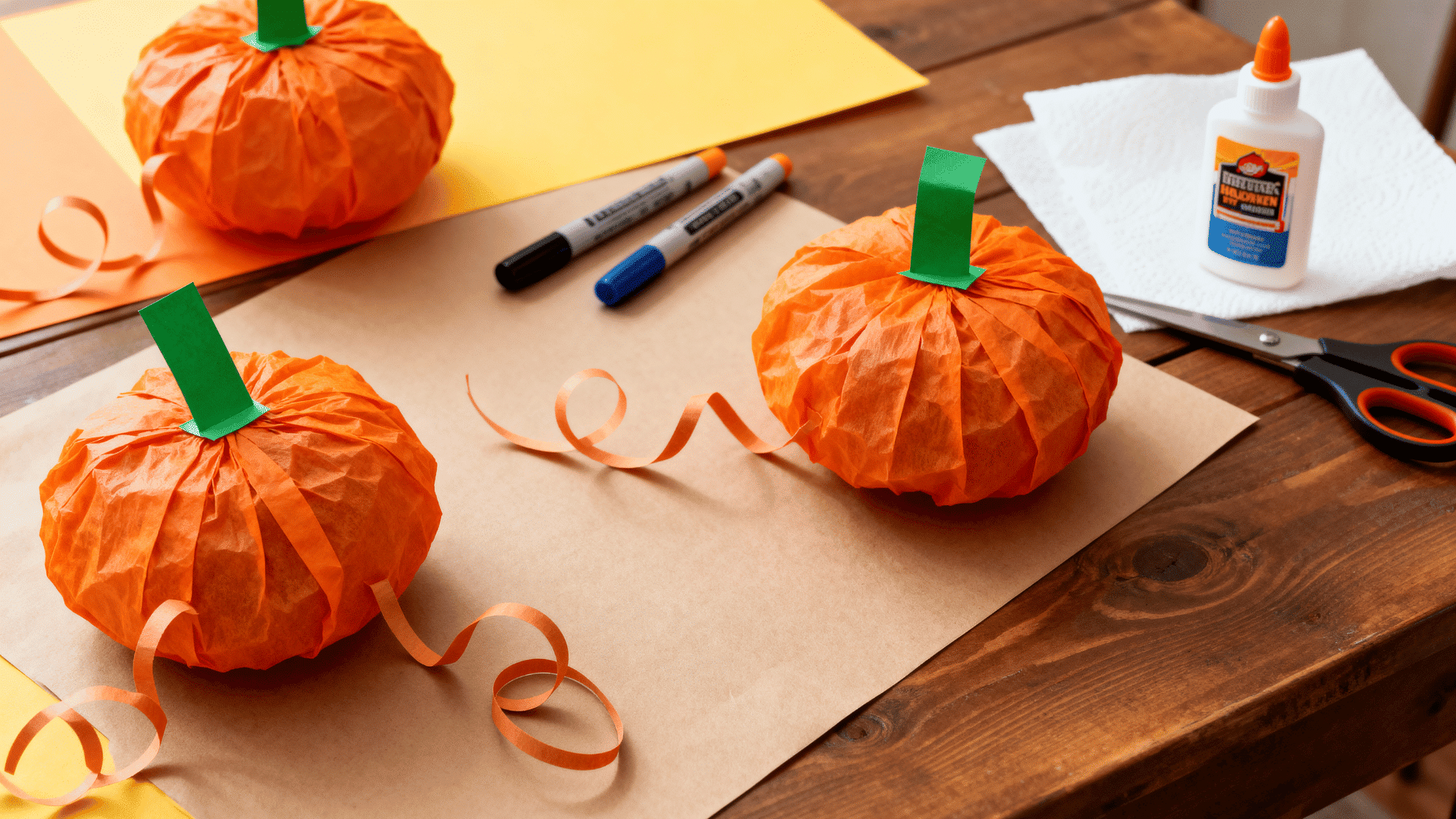 orange coffee filter pumpkins with paper stems and vines on a fall craft table with markers and scissors nearby